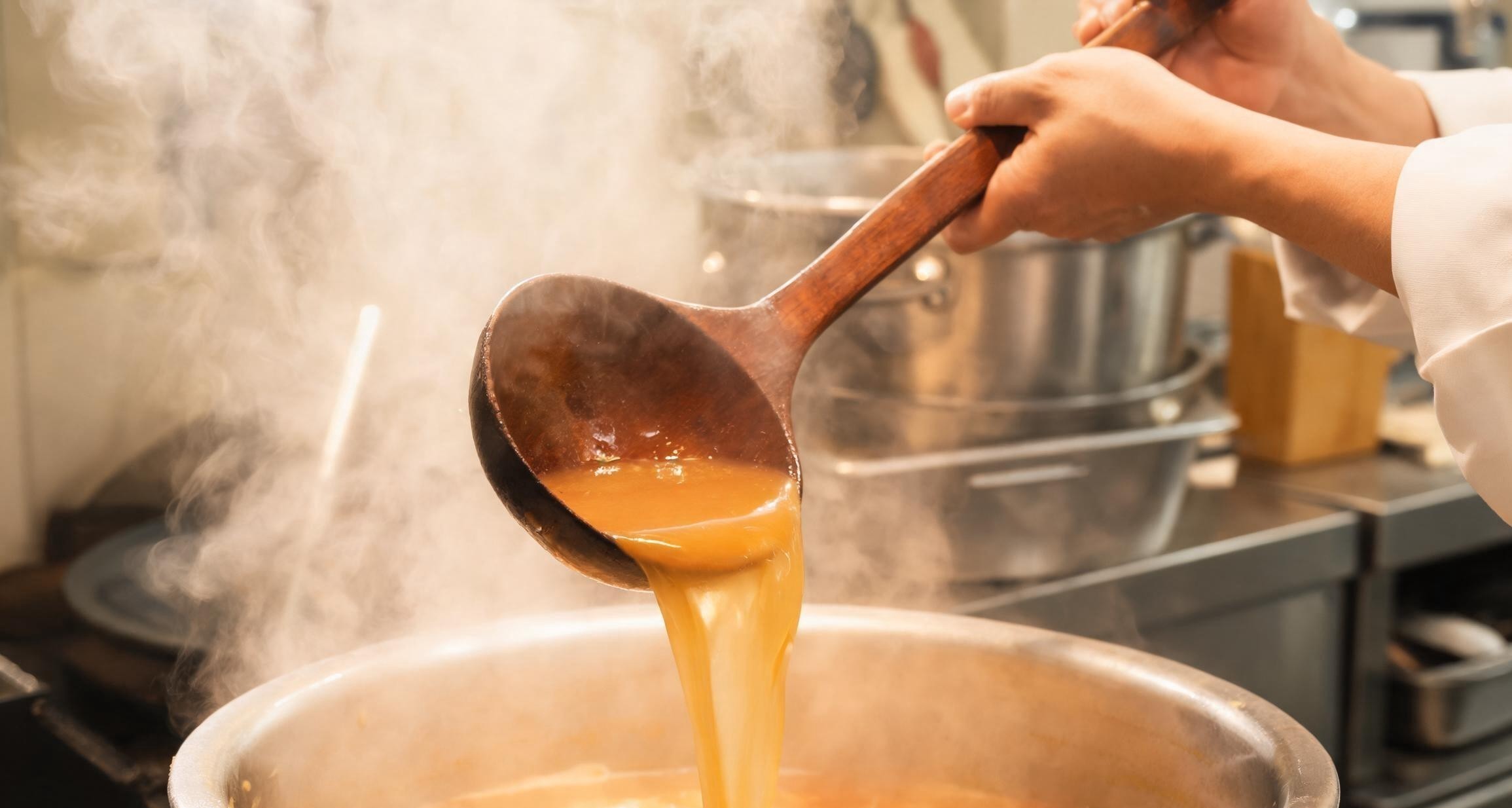 A close-up of milky tonkotsu ramen broth being ladled into a bowl